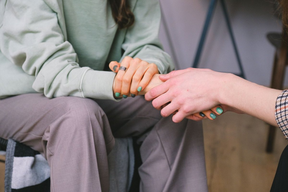 One person gently holding another person’s hands in support